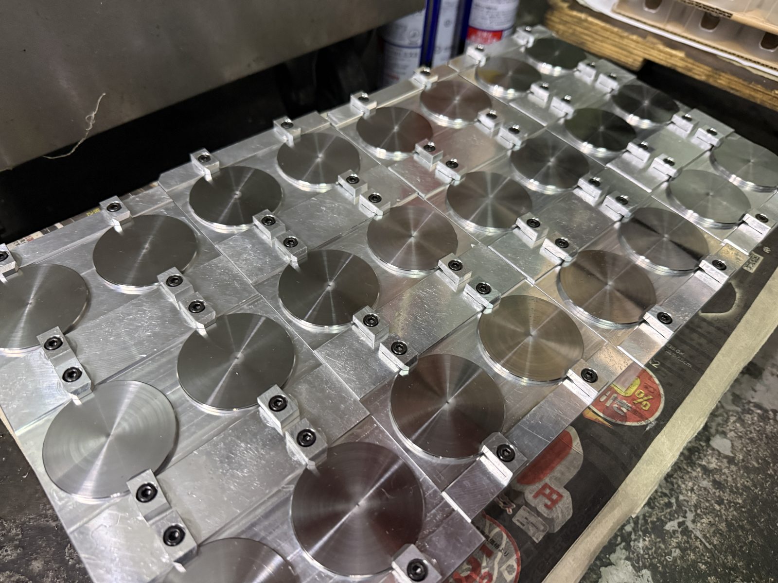 板材の治具に多数の丸物部品をクランプで固定し、穴あけ加工を行う多数個取りの段取り